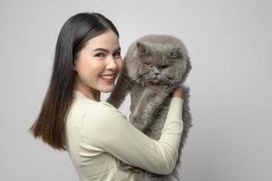 una mujer joven está sosteniendo un gato adorable, jugando con un gato en un estudio de fondo blanco foto