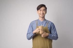 Portrait of young asian man wearing apron holding paper cup over white background studio, Save earth concept. photo