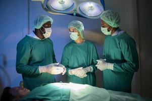 Group of mixed-races professional surgeons operating in hospital operating room , health care concept. photo