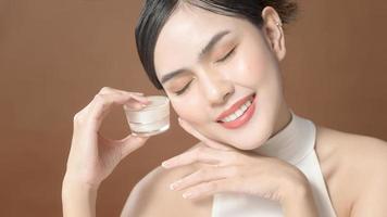 A young woman with beautiful face is holding cream , using cream of her face , beauty skin care concept photo