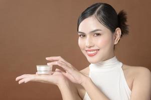 A young woman with beautiful face is holding cream , using cream of her face , beauty skin care concept photo