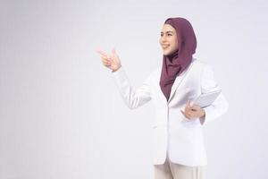 Beautiful muslim business woman wearing white suit with hijab holding tablet in studio photo