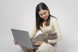 A Scottish fold lovely cats lying on  young woman hand while working with laptop computer on white studio background photo