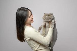 una mujer joven está sosteniendo un gato adorable, jugando con un gato en un estudio de fondo blanco foto