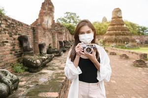 young beautiful woman wearing protective mask traveling and taking photo at thai historical Park, Holidays and cultural tourism concept.