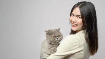 una mujer joven está sosteniendo un gato adorable, jugando con un gato en un estudio de fondo blanco foto