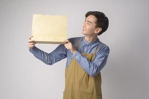 Portrait of young asian man wearing apron holding paper bag over white background studio, Save earth concept. photo