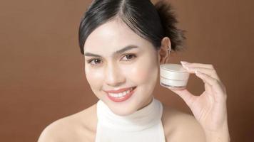 A young woman with beautiful face is holding cream , using cream of her face , beauty skin care concept photo