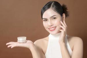 A young woman with beautiful face is holding cream , using cream of her face , beauty skin care concept photo