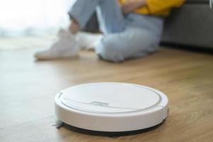 Young happy woman using Robotic vacuum cleaner in living room photo
