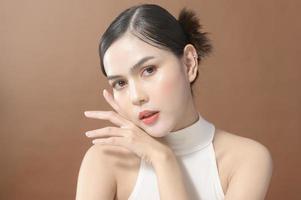 A young woman with beautiful face smiling , touching her face over brown background , beauty skin care concept photo