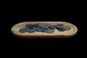 Coins of different value on a wooden plate on a black background. photo