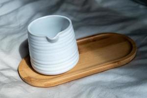 Mug made of white clay or ceramic mug on the wooden plate, the cloth background and natural light. photo