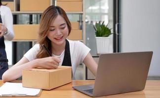 Portrait of Asian young woman SME working with a box at home the workplace.start-up small business owner, small business entrepreneur SME or freelance business online and delivery concept. photo