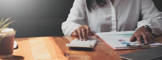 primer plano de las manos de una mujer de negocios usando una calculadora para verificar las finanzas, las ganancias y el presupuesto de la empresa. mujer de negocios calculando gastos mensuales, gestionando presupuesto, papeles, documentos de préstamo, facturas. foto