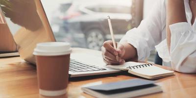 Close up image of a woman writing and taking note on notebook with laptop in office. photo