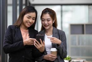 Two asian businesswoman in formal suit in office happy and cheerful during using smartphone and working in the office. photo