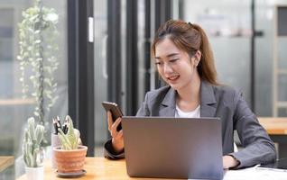 Asian businesswoman in formal suit in office happy and cheerful during using smartphone and working photo