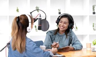 Smile two asian young woman, man radio hosts in headphones, microphone while talk, conversation, recording podcast in broadcasting at studio together. Technology of making record audio concept. photo