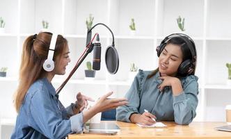 Smile two asian young woman, man radio hosts in headphones, microphone while talk, conversation, recording podcast in broadcasting at studio together. Technology of making record audio concept. photo