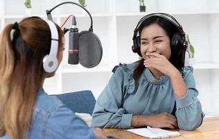 Smile two asian young woman, man radio hosts in headphones, microphone while talk, conversation, recording podcast in broadcasting at studio together. Technology of making record audio concept. photo