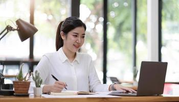 Beautiful young asian woman sitting at coffee shop using laptop. Happy young businesswoman sitting at table in cafe with tab top computer. photo