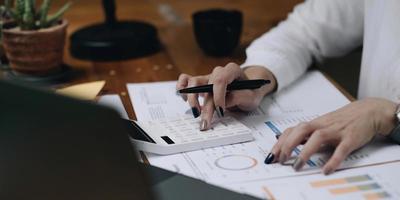 Mujer de negocios de cerca con calculadora y computadora portátil para hacer finanzas matemáticas en un escritorio de madera en la oficina y el fondo de trabajo empresarial, impuestos, contabilidad, estadísticas y concepto de investigación analítica foto