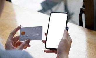 pago en línea. mujer sosteniendo un teléfono inteligente con pantalla en blanco y tarjeta de crédito, haciendo transacciones financieras foto
