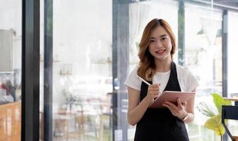 Portrait, Beautiful millennial Asian female waitress or restaurant owner standing in front of her restaurant entrance. Restaurant or coffee shop business owner concept. photo