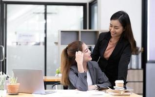 un hombre de negocios asiático presenta y explica el trabajo a una colega, usando una computadora portátil en la oficina por la noche. trabajo en equipo, cooperación entre compañeros de trabajo, equipo de marketing financiero o concepto de negocio corporativo. foto