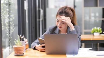 una joven empresaria asiática seria en el escritorio de su oficina lidiando con un problema de teléfono inteligente o recibiendo un correo electrónico de queja de su jefe. foto