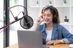 Woman recording a podcast on her laptop computer with headphones and a microscope. Female podcaster making audio podcast from her home studio. photo