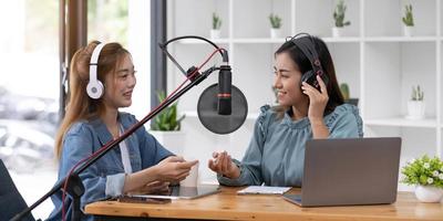 Smile two asian young woman, man radio hosts in headphones, microphone while talk, conversation, recording podcast in broadcasting at studio together. Technology of making record audio concept. photo