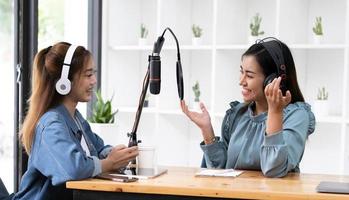 Smile two asian young woman, man radio hosts in headphones, microphone while talk, conversation, recording podcast in broadcasting at studio together. Technology of making record audio concept. photo