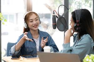 Smile two asian young woman, man radio hosts in headphones, microphone while talk, conversation, recording podcast in broadcasting at studio together. Technology of making record audio concept. photo