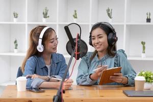 Smile two asian young woman, man radio hosts in headphones, microphone while talk, conversation, recording podcast in broadcasting at studio together. Technology of making record audio concept. photo