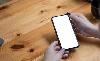 mujer de la mano usando un teléfono, un teléfono inteligente de pantalla vacía y una computadora en la vista superior de la mesa de madera. foto