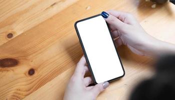 mujer de la mano usando un teléfono, un teléfono inteligente de pantalla vacía y una computadora en la vista superior de la mesa de madera. foto