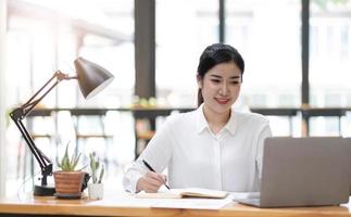 Beautiful young asian woman sitting at coffee shop using laptop. Happy young businesswoman sitting at table in cafe with tab top computer. photo