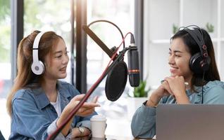 Smile two asian young woman, man radio hosts in headphones, microphone while talk, conversation, recording podcast in broadcasting at studio together. Technology of making record audio concept. photo