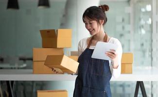 Startup SME small business entrepreneur SME or freelance Asian woman using a laptop with box, Young success Asian woman with her hand lift up, online marketing packaging box and delivery, SME concept. photo