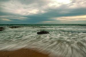 impresionante paisaje marino de larga exposición con olas que fluyen entre rocas al atardecer foto