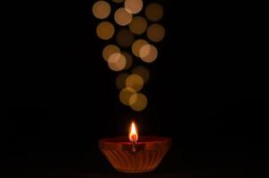 Selective focus on flame of clay diya lamp lit on dark background with bokeh lights. Diwali festival concept. photo