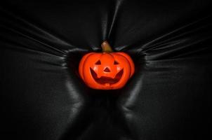 calabaza de halloween sosteniendo a mano presionando a través de fondo de tela negra. concepto de festival de halloween. foto