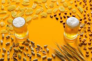 Two glasses of beer with chips and nuts on yellow background for Oktoberfest concept. photo