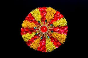 Decorative marigold and rose flower petals rangoli for Diwali festival with diya lamp lit with blurred focus flame on black background. photo