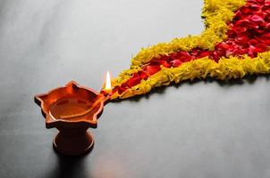 lámpara diya de arcilla con caléndula decorativa y pétalos de flores de rosa rangoli en el suelo para el festival diwali. foto