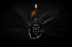 Black candle with flame on skull holding by hand pressing through black fabric background. Halloween festival concept. photo