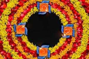 Decorative marigold and rose flower petals rangoli for Diwali festival with clay diya lamps lit with blurred focus flame on black background. photo