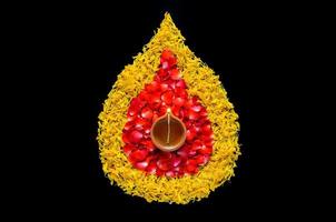 Decorative marigold and rose flower petals rangoli for Diwali festival with clay diya lamp lit with blurred focus flame on black background. photo